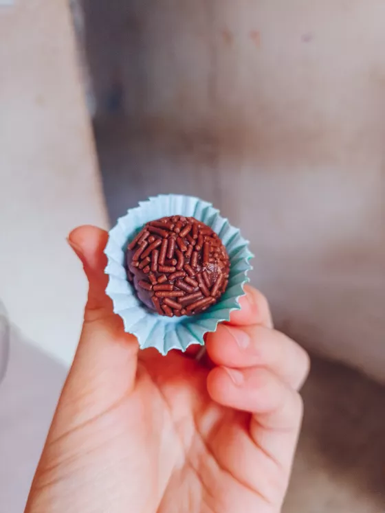 Brigadeiro de chocolate em forminha azul claro sendo seguro em uma mão